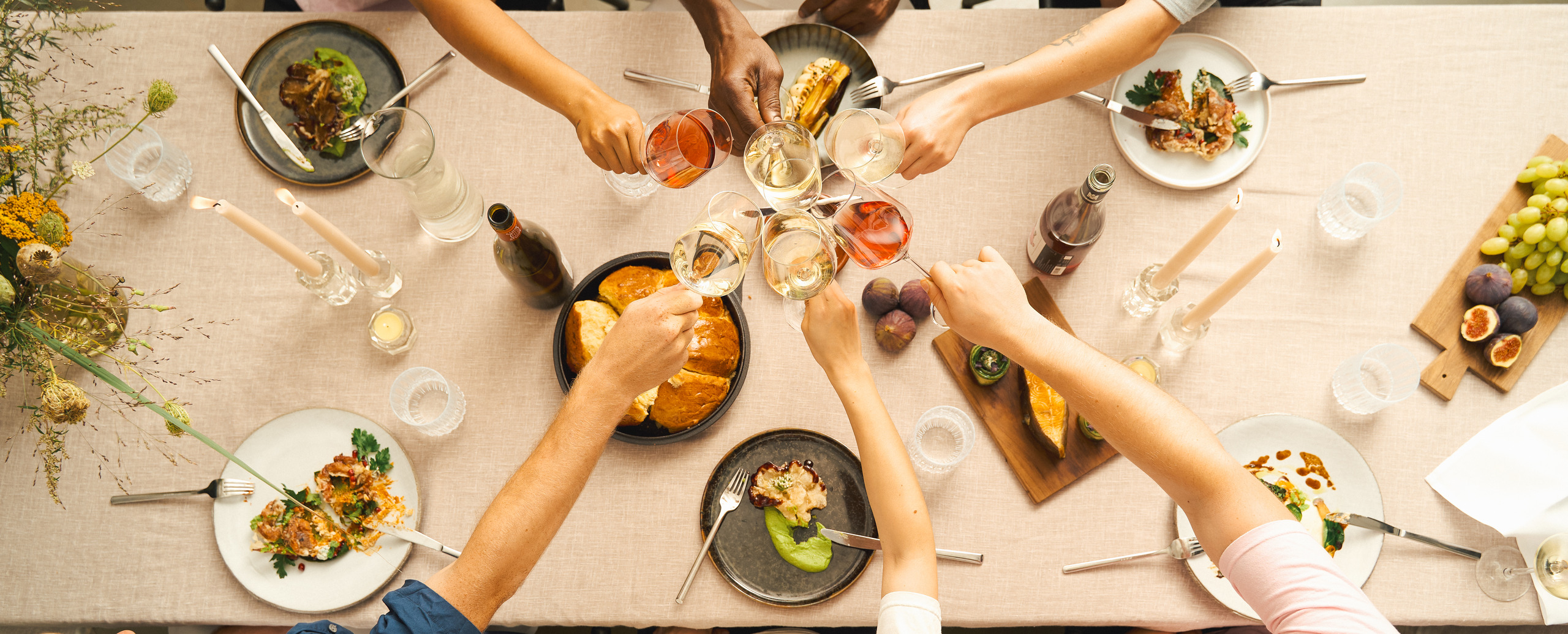 Overhead view of hands toasting glasses around a laid table